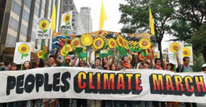 People marching behind a banner that says Peoples Climate March