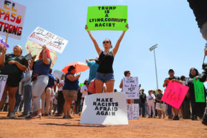 Woman holding up a sign that says "Trump is a lying corrupt racist"