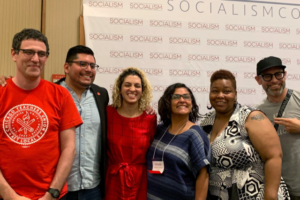 6 people posing for a group photo with a slide about socialism in the background