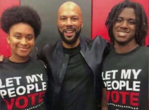 Two black women with a black man standing between them. The women are wearing tshirts that say "Let my people vote"