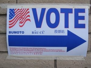 Photo of a sign that says Vote with a large blue arrow