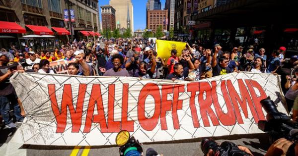 People at a protest marching behind a banner that says Wall Off Trump