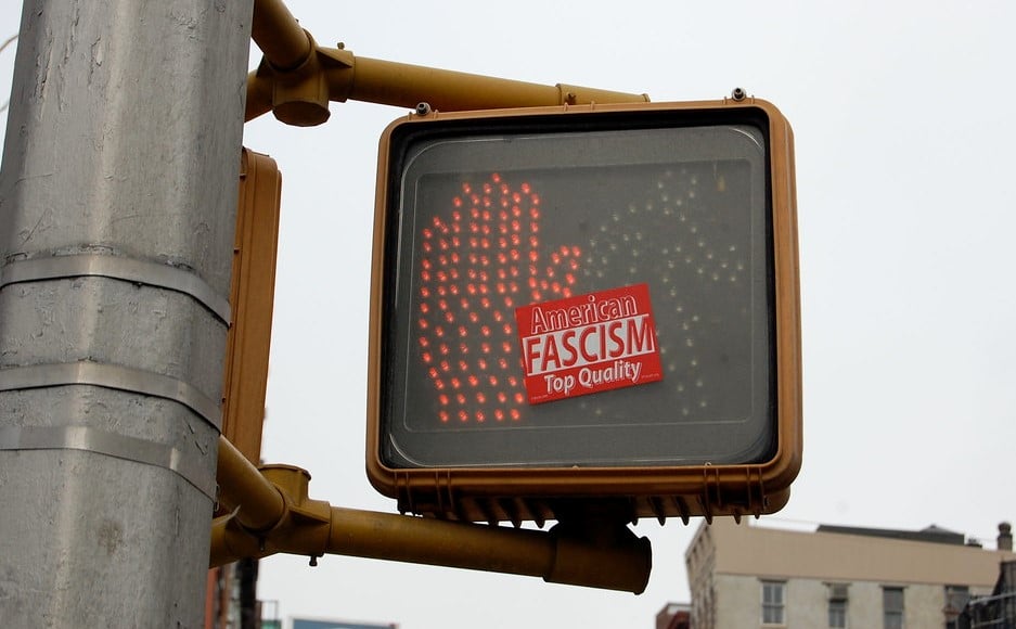 Photo of a don't walk sign with sticker next to it that says "facism"
