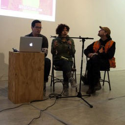Murkey photo of three people sitting in chairs with a microphone in front of them