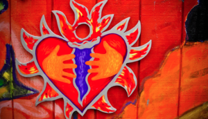 Image of stained glass red heart with a blue cone holding a flame reminiscent of the olympic flame