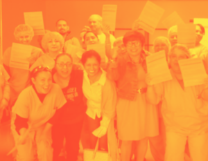 A group of people smiling triumphantly, holding pieces of paper. Most are women; many wear scrubs and puffy shower-cap type covers on their heads.