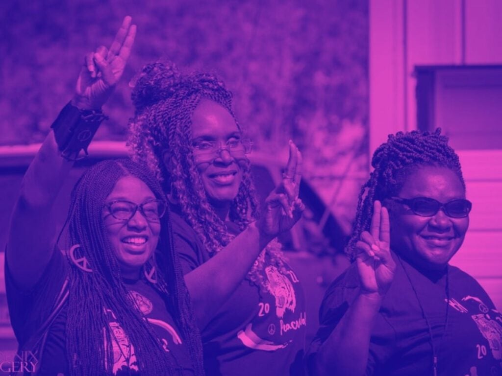Close-up of three Black women smiling, making a closed-finger peace sign.
