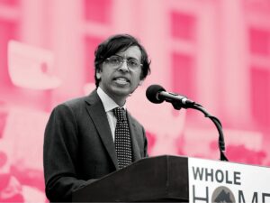 A black and white photo of Senator Nikil Saval stands at a podium that reads "Whole Home" on the front superimposed over a pink tinted croud of people