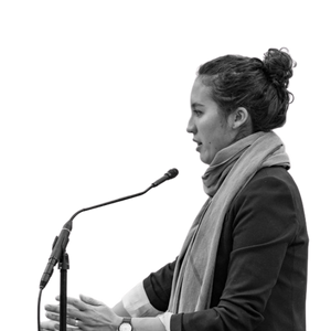 Black and white photo of Emma Tai standing at a podium mid speech