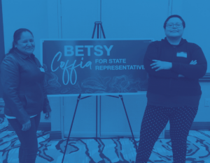 Two Latinas standing on either side of a sign that reads "Betsy Coffia for State Representative."